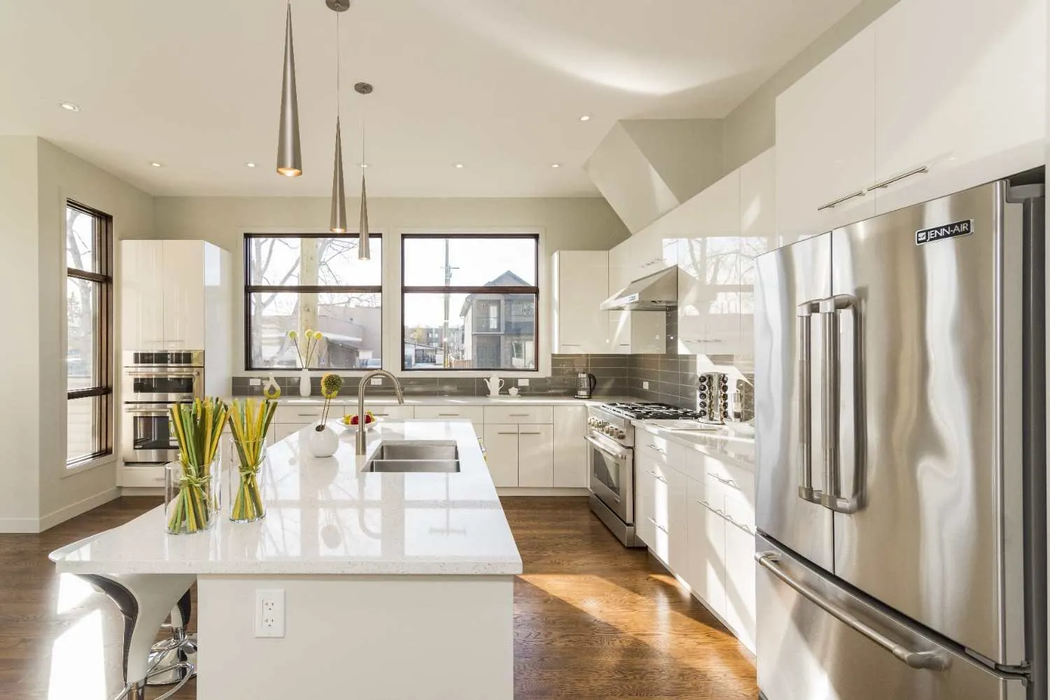 Bright kitchen with a steel refrigerator, gas range, wall ovens and a sink island